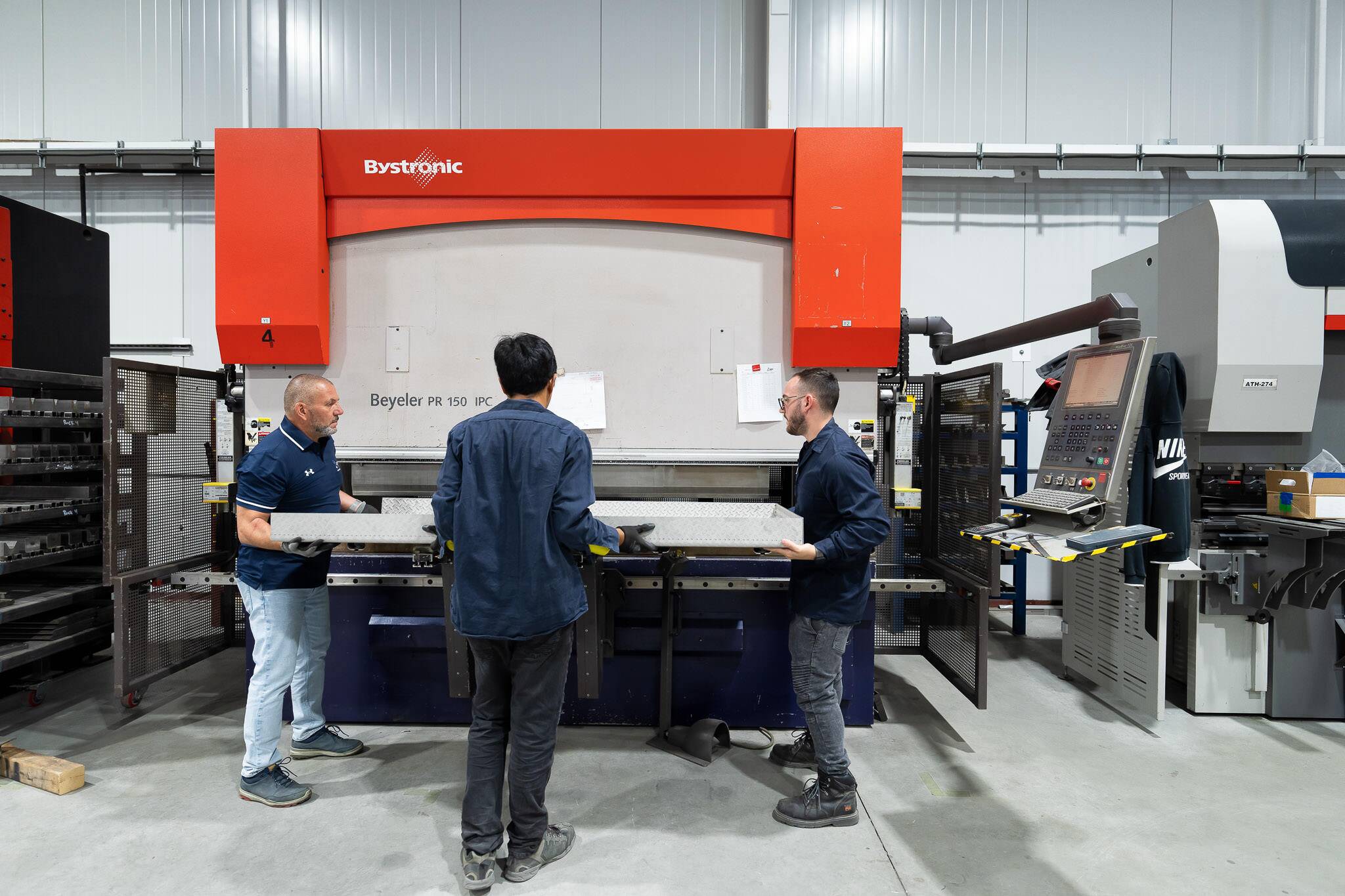 "ATH employees collaborating near a Bystronic press brake machine in a metal workshop"